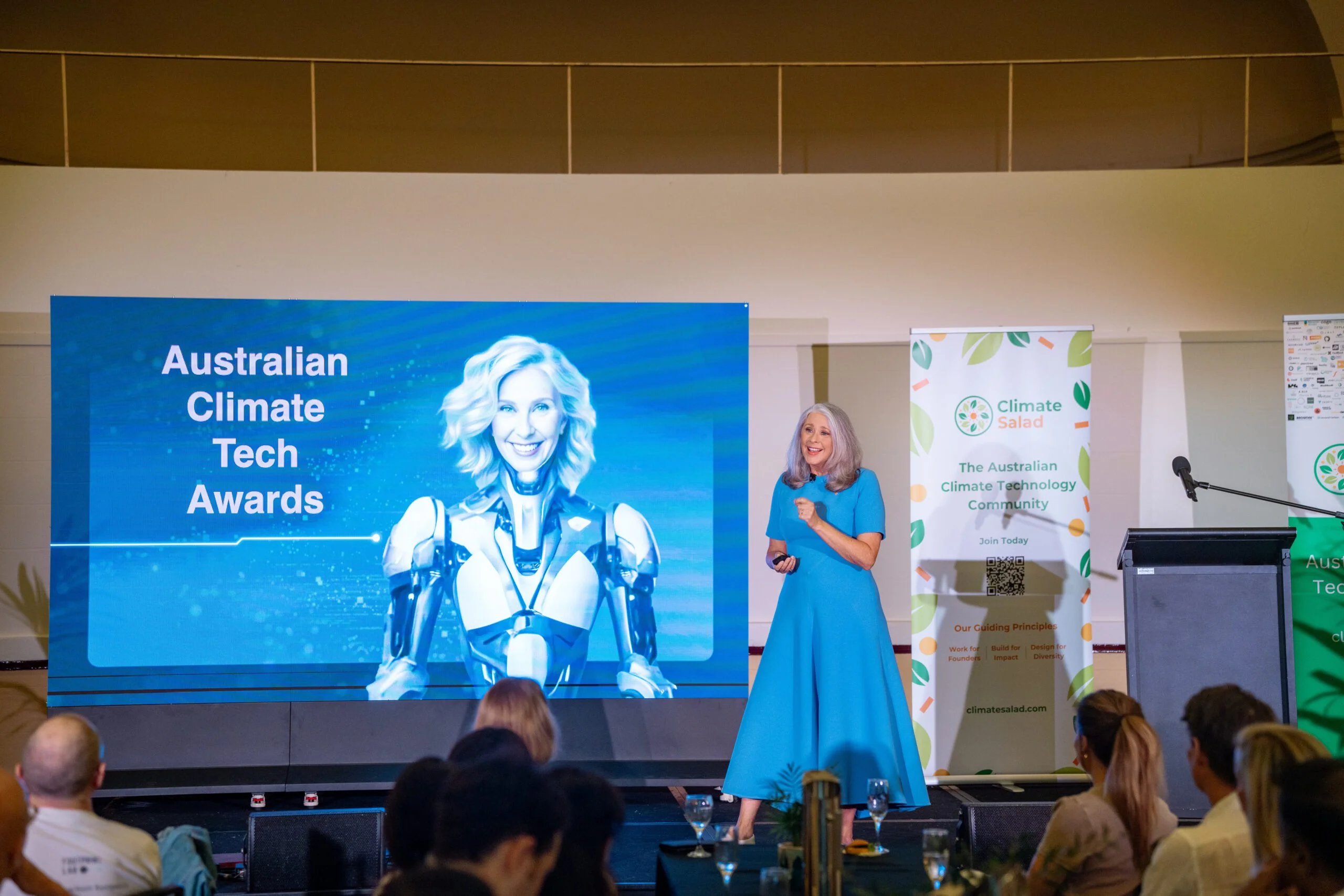 A female speaker in a blue dress presenting at the Australian Climate Tech Awards.