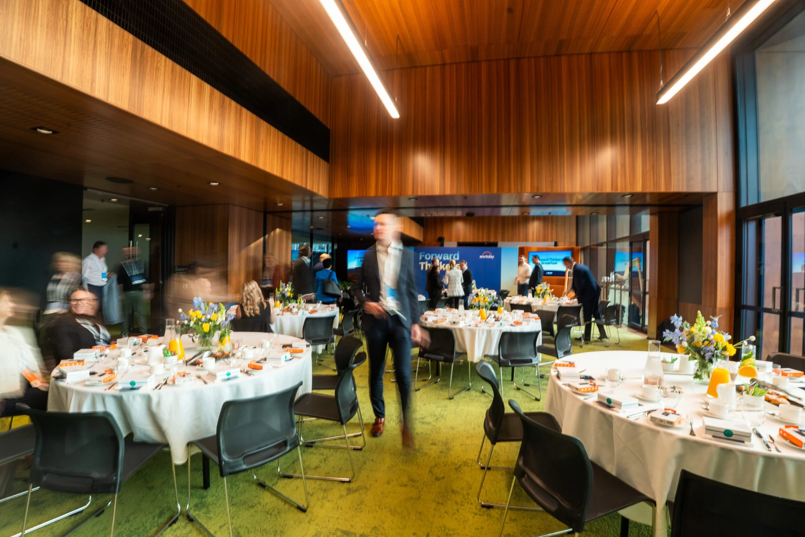 A corporate breakfast summit event set up with round tables in a warm, wood-panelled venue.