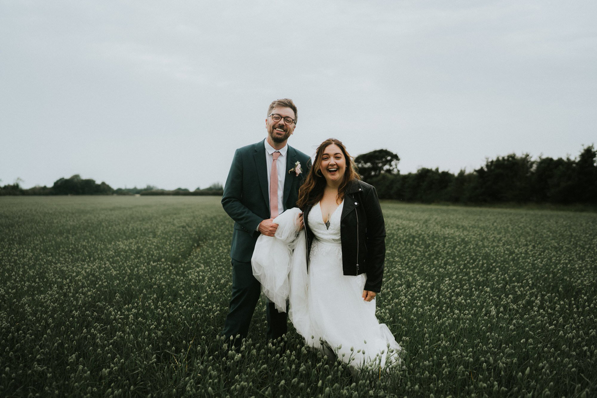 A newly married couple laughing together in an open countryside field.