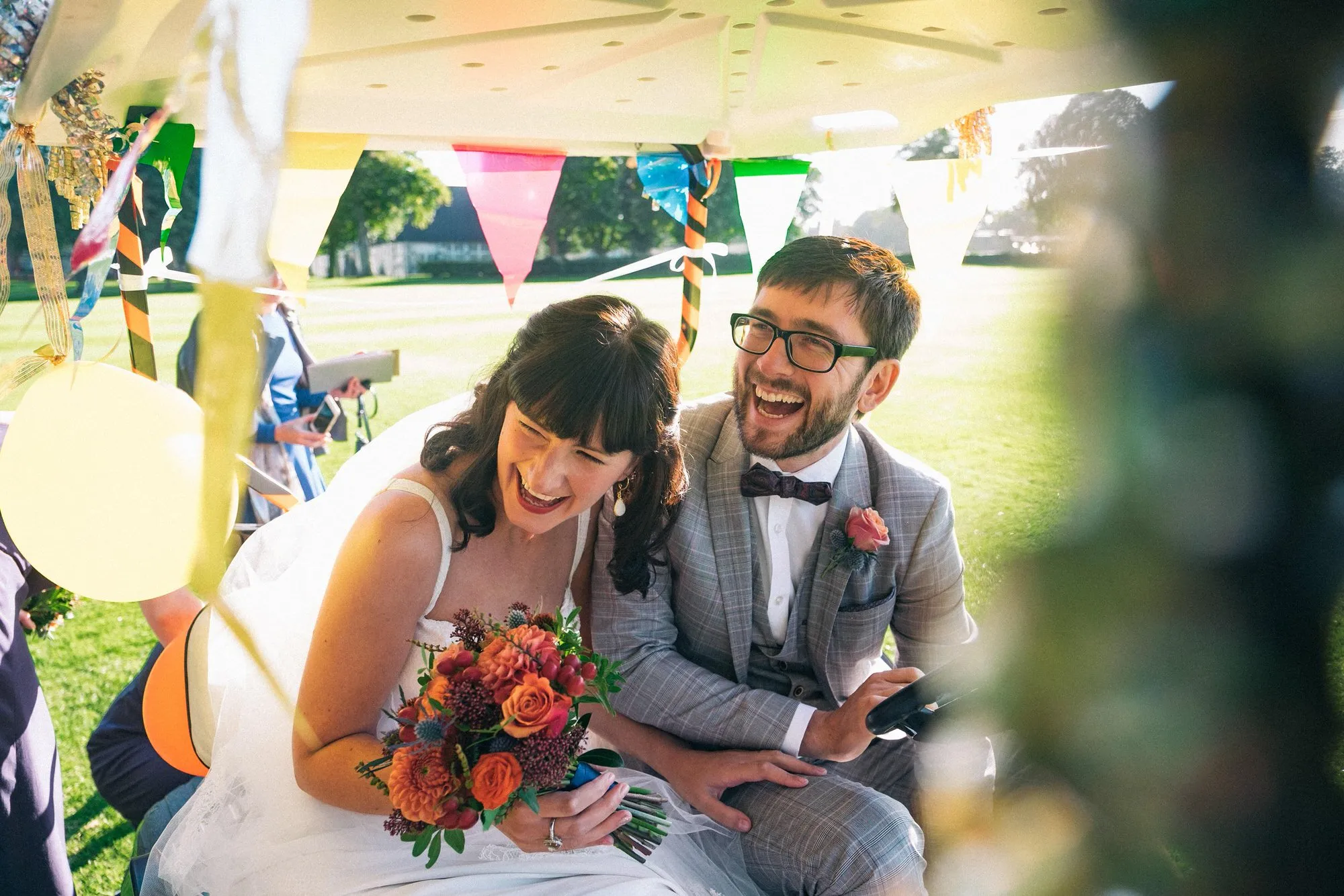 Newlyweds laughing together inside a bunting-decorated golf buggy.