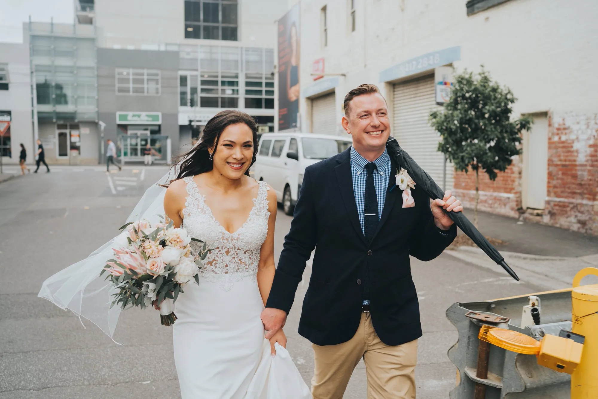 Newlyweds walking hand in hand through a Sydney city street.