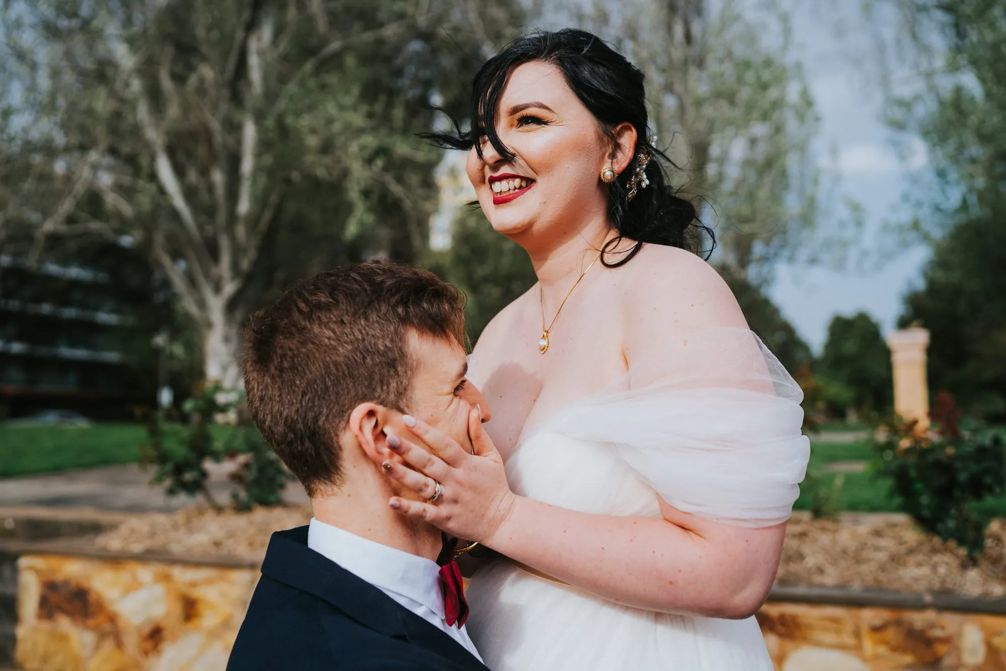 A joyful bride laughing with her partner in a sunlit Sydney park.