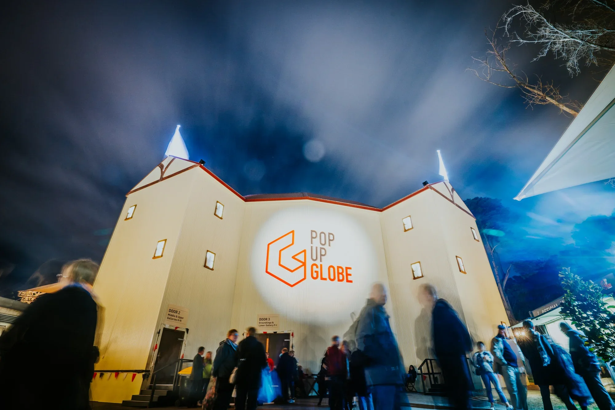 Pop Up Globe Sydney event photography: Illuminated venue exterior at night with attendees gathering outside.